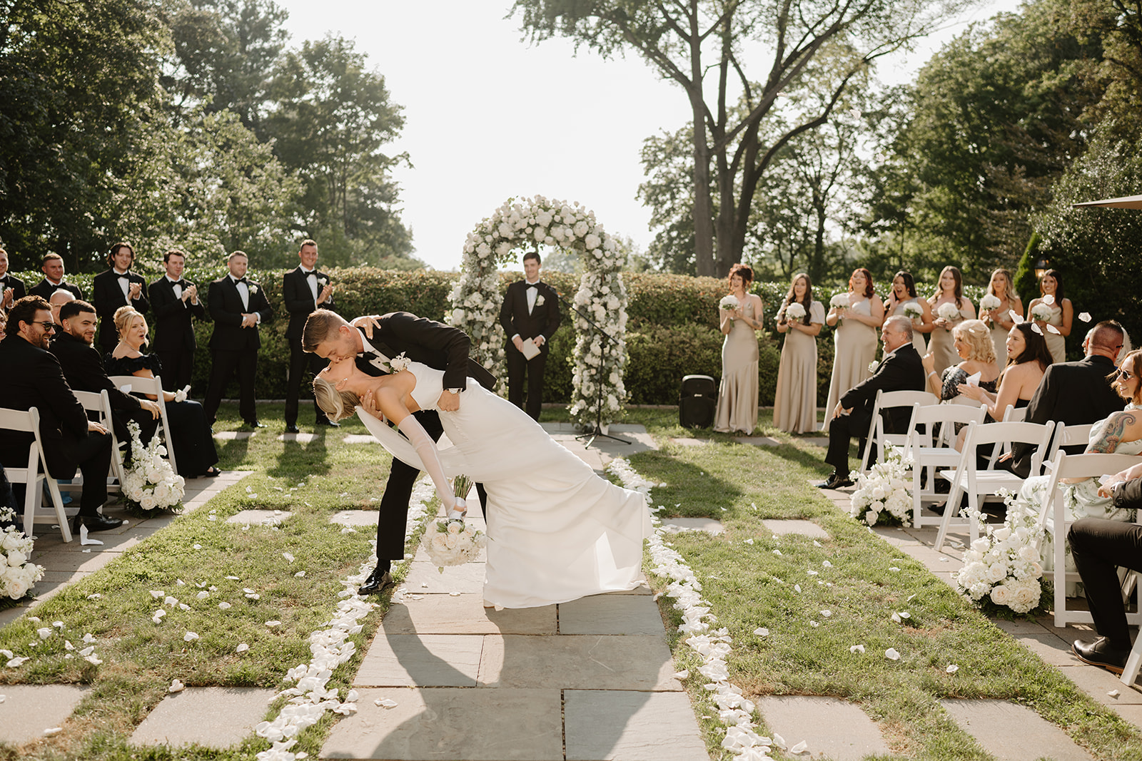 Groom dips and kisses the bride on the petal-strewn aisle as guests cheer during the recessional.